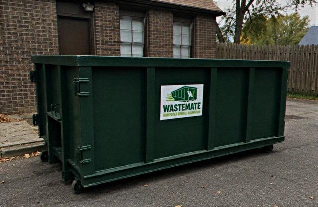Green dumpster beside a brick home during a renovation