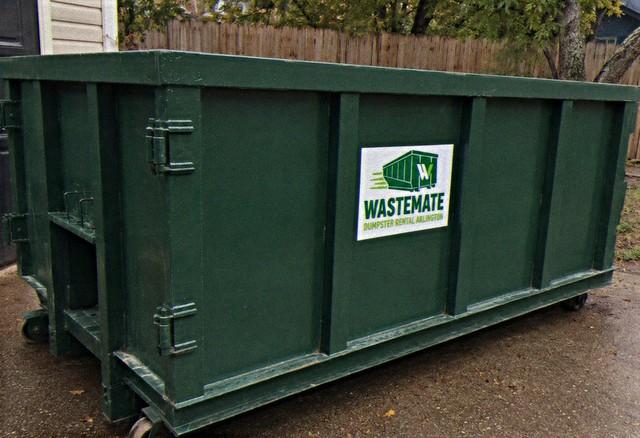 Dumpster positioned in a driveway beside a wooden fence